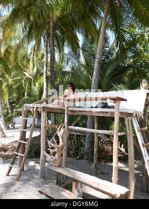 Frau, 45, trinken einen Cocktail auf eine Sitzerhöhung in einer Strandbar unter Palmen Bäume, Playa Samara, Halbinsel Nicoya, Costa Rica Stockfoto