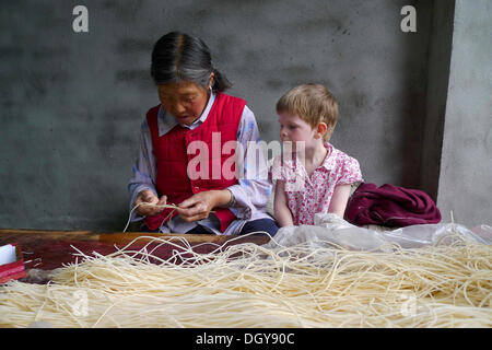 Begegnungen in China, europäische Mädchen beobachten auf alte chinesische Frau machen Räucherstäbchen, Moxi, Hailuogou, Sichuan, China Stockfoto