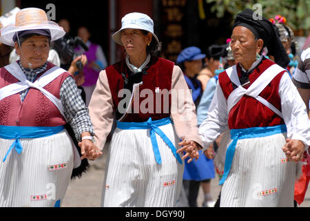 Drei Frauen in Tracht der Naxi-Minderheit Hand in Hand und tanzen auf dem Hauptplatz in Lijiang, Yunnan Stockfoto