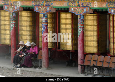 Drei alte tibetische Frauen sitzen vor der großen Gebetsmühlen des Lhagang Klosters, Lhagang Gompa, Tagong, Sichuan Stockfoto