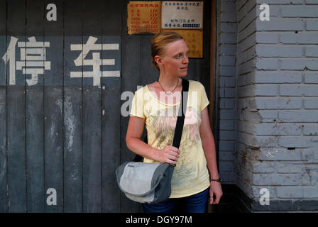 Rothaarige Frau, die ein Umhängetasche steht vor einem Haus auf einem chinesischen Hutong, eine schmale Straße Stockfoto