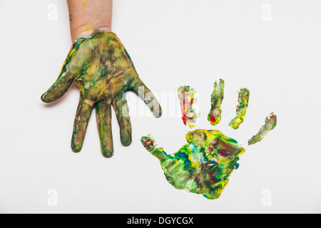 Kind mit bunt bemalten Hand neben ihrem Handabdruck auf Papier Stockfoto