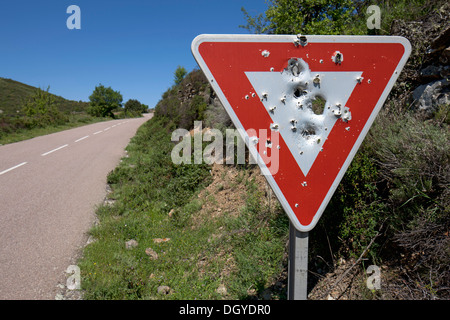 Ein Ertrag Zeichen mit Einschusslöchern in es geschrieben auf einer abgelegenen Landstraße Stockfoto