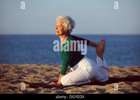 Ältere Frau in stretching Lage am Meer am Morgen. Ältere Frau beim Yoga am Strand. Stockfoto