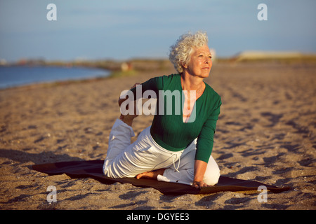 Ältere Frau in stretching Lage am Meer am Morgen. Ältere Frau beim Yoga am Strand. Stockfoto