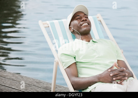 Glücklicher Mann auf Deck Chair von See mit Kopfhörern Stockfoto