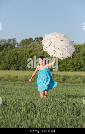 Ein junges Mädchen einen Regenschirm halten während des Durchlaufs durch ein Feld im Sommer Stockfoto