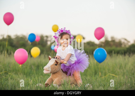 Ein kleines Mädchen mit Tutu auf einem Schaukelpferd in einem Feld mit Luftballons Stockfoto