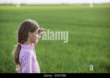 Ein junges Mädchen in einem Feld stehen, anzeigen, Abschirmung ihre Augen und schauen Stockfoto