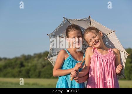 Lachende Zwillingsschwestern stehend in einem Feld unter einem Regenschirm Stockfoto