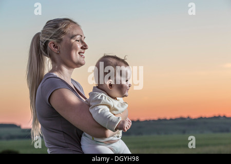 Eine lachende Frau hält ihr Baby in einer natürlichen Umgebung