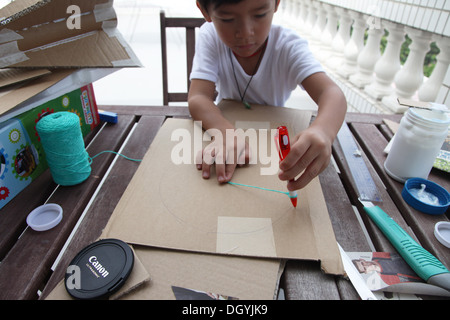 Es ist ein Foto von einen kleinen asiatischen Jungen Whi tut DIY arbeiten mit Karton, eine Rakete zu tun. Er schneidet, Pasten und malt es. Er ist pro Stockfoto