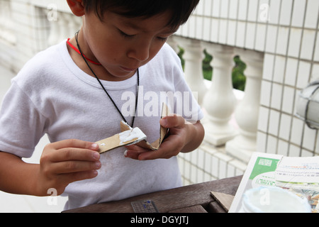 Es ist ein Foto von einen kleinen asiatischen Jungen Whi tut DIY arbeiten mit Karton, eine Rakete zu tun. Er schneidet, Pasten und malt es. Er ist pro Stockfoto