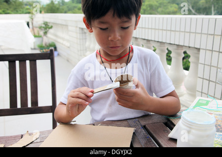 Es ist ein Foto von einen kleinen asiatischen Jungen Whi tut DIY arbeiten mit Karton, eine Rakete zu tun. Er schneidet, Pasten und malt es. Er ist pro Stockfoto