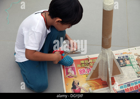 Es ist ein Foto von einen kleinen asiatischen Jungen Whi tut DIY arbeiten mit Karton, eine Rakete zu tun. Er schneidet, Pasten und malt es. Er ist pro Stockfoto