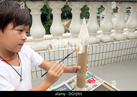 Es ist ein Foto von einen kleinen asiatischen Jungen Whi tut DIY arbeiten mit Karton, eine Rakete zu tun. Er schneidet, Pasten und malt es. Er ist pro Stockfoto