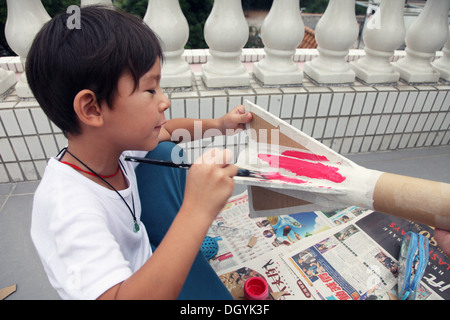 Es ist ein Foto von einen kleinen asiatischen Jungen Whi tut DIY arbeiten mit Karton, eine Rakete zu tun. Er schneidet, Pasten und malt es. Er ist pro Stockfoto