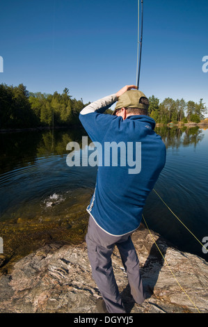 Ein Mann spielt einen Fisch von einem Felsen-Punkt im Algonquin Park, Kanada Stockfoto