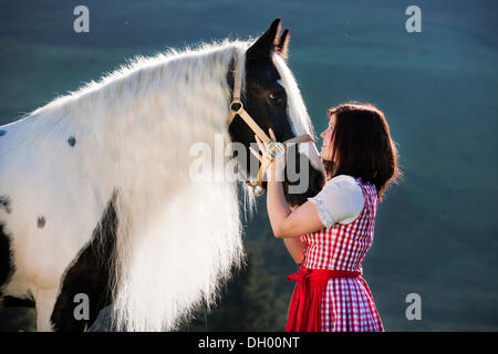 Junge Frau trägt ein Dirndl kuscheln mit einem Gypsy Vanner oder Tinker Pferd, Pinto, schwarz und weiß, Nord-Tirol, Austria, Europe Stockfoto