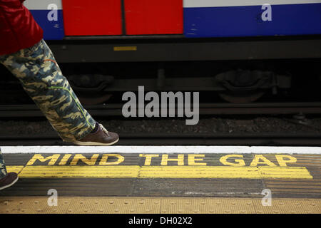 Gelbe Markierung MIND THE GAP auf dem Boden einer Station der London Underground, Hose eine Person trägt militärische einen Schritt Stockfoto