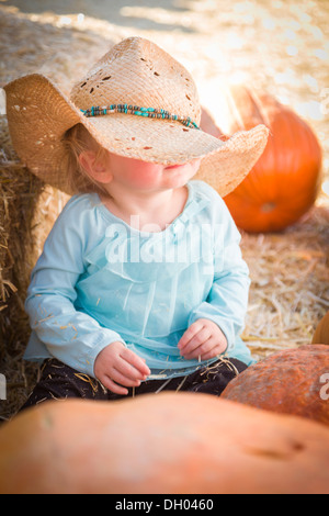 Entzückende Babymädchen mit Cowboy-Hut in einer rustikalen Landschaft auf dem Kürbisfeld. Stockfoto