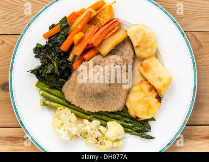 Traditionelle britische Sonntag Mittagessen - Roastbeef, geröstete Kartoffeln, Karotten, Pastinaken, Grünkohl, Spargel und Blumenkohl auf einer Platte Stockfoto