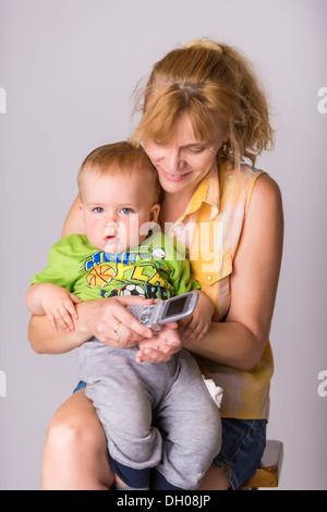 Ein Junge zwischen 1 und 2 Jahren auf Schoß einer reifen Frau, einem jungen Großmutter, die versucht, einen Handy-Anruf initiieren. Stockfoto