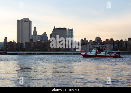 Lower East Side Nachbarschaft von zwei Brücken in der Dämmerung mit einem FDNY Boot am East River in New York, NY, USA im Oktober 2012. Stockfoto