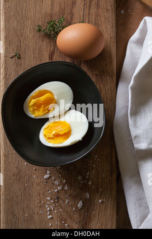 Ein hart gekochtes Ei in schwarz Schüssel auf Holzbrett Stockfoto