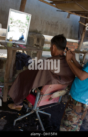 Ein Friseur gibt einem Mann einen Haarschnitt in einem Barbershop auf einer Stadtstraße in Kampong Cham, Kambodscha. Stockfoto