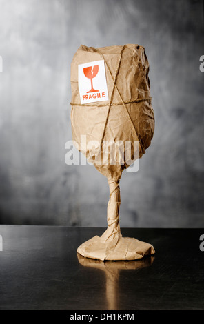 Ein Glas Wein mit "Fragile" Warnaufkleber in braunem Packpapier verpackt. Stockfoto