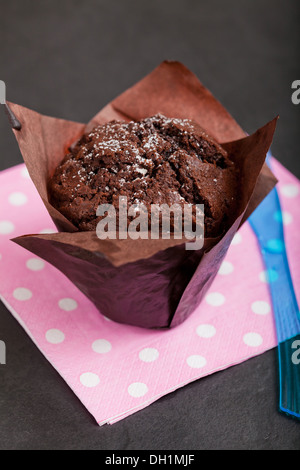 Nahaufnahme von Schoko-Muffin bestreut mit Puderzucker ruht auf rosa Serviette mit weißen Flecken Stockfoto