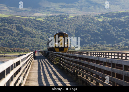 Arriva Trains Wales Dienst auf der Cambrian Küstelinie nähert sich über Barmouth Brücke; Hügeln und Wäldern im Hintergrund Stockfoto