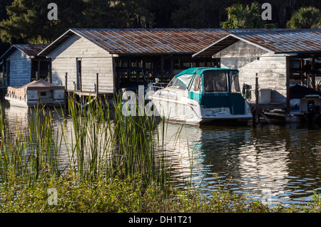 Boote und Motoryacht mit türkisfarbenen Baldachin vor Anker von Bootshäusern, See Dora, Mount Dora, Florida USA Stockfoto