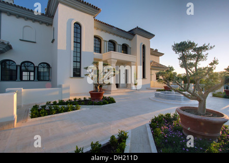 Cloud-beschnittene Sträucher in Töpfen unter gepflanzt mit kleinen Stauden in Betten Marmor Pflaster vor große Villa in Spanien Stockfoto