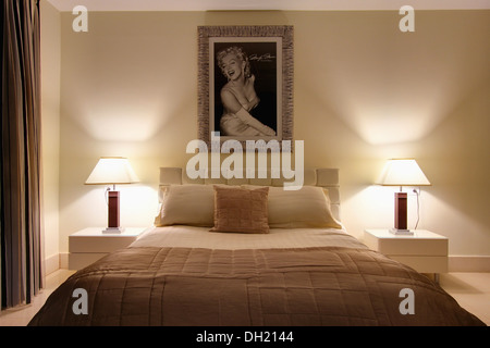 Gerahmte Bild von Marilyn Monroe über Bett mit Beige Quilt in modernen Schlafzimmer mit brennenden Lampen auf den Tischen entweder Seite des Bettes Stockfoto