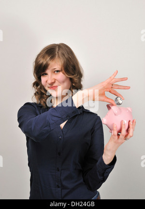Junge Frau, 20, eine 10 Euro Silber Münze in ein rosa Sparschwein Stockfoto