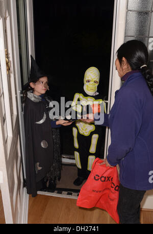Zwei junge Kinder "Süßes oder Saures", gekleidet im Kostüm Halloweenkostüme in offenen Tür des Hauses. Bewohner des Hauses ist verbindlich und reichte ein "Leckerbissen" für dem jungen Mädchen, gekleidet wie eine Hexe. Bildnachweis: Rsdphotography/Alamy Live-Nachrichten Stockfoto
