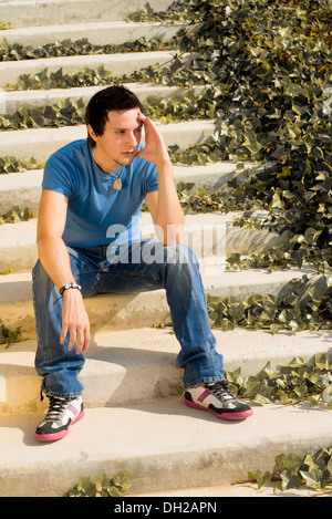 Junger Kerl in nachdenkliche Haltung sitzt auf einer Treppe Stockfoto