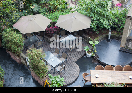 Haus Terrasse mit Tisch und Stühlen unter Dach, gibt es eine Menge Vegetation rund um. Stockfoto