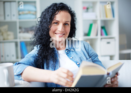 Glücklich Brünette in Freizeitkleidung Buch zu Hause Stockfoto