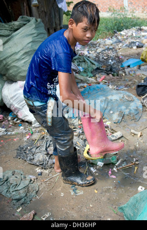 Ein kleiner Junge ist anders farbige Stiefel tragen, während der Arbeit an einem Müll recycling Depot in Phnom Penh, Kambodscha. Stockfoto