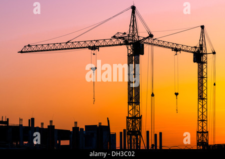 Industrielle Baukräne und Gebäude Silhouetten über Sonne bei Sonnenuntergang Stockfoto