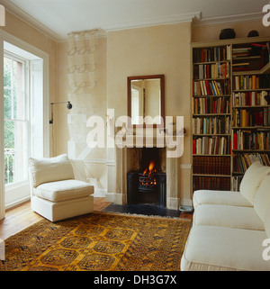 Weißer Stuhl und Sofa in weiß Wohnzimmer mit gelb gemusterten Orientteppich georgischen Kamin mit dem brennenden Feuer Stockfoto