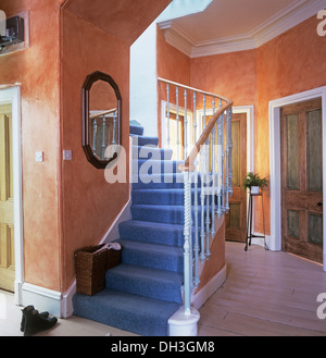 Blauer Teppich auf Treppe in hellorange Waschungen Wirkung Halle mit lackiertem Holzboden Stockfoto