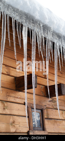 Holzhaus mit großen Eiszapfen auf schneebedeckten Dach Stockfoto