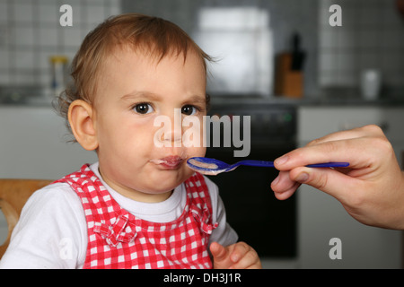 Kleines Mädchen essen Brei, seine Mutter füttert ihr Stockfoto