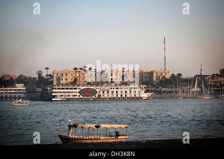 Kreuzfahrtschiff Verankerung vor dem traditionellen Winter Palace Hotel, gesehen aus dem Westjordanland über den Nil bei Luxor, Ägypten Stockfoto