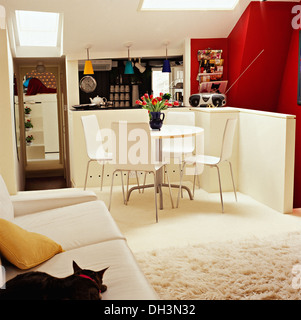 Katze sitzt auf weißen Sofa im Essbereich des modernen Konvertierung Loftwohnung mit Schaffell Teppich und weiße Tisch und Stühlen Stockfoto