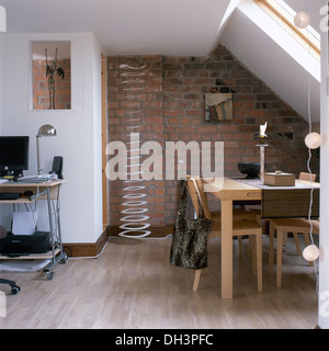 Blasse Holztisch und Stühle im Essbereich des kleinen Dachgeschossausbau mit Metallspirale Skulptur gegen Backstein-Mauer Stockfoto